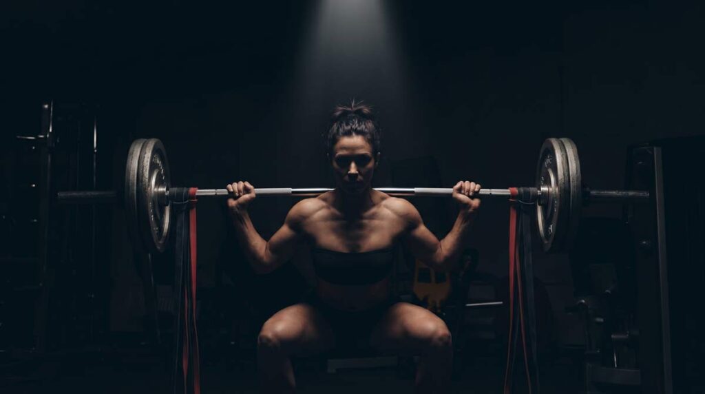 Atleta de powerlifting realizando agachamento com elásticos na barra em academia